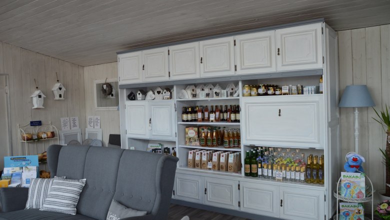 Interior view of a cozy store with white shelves filled with drinks and products. A gray sofa stands in the foreground.