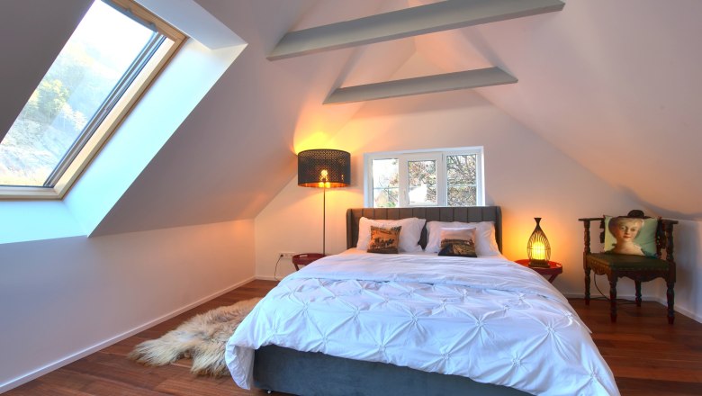 Modern bedroom with sloping ceiling, large bed, skylight and stylish lighting.