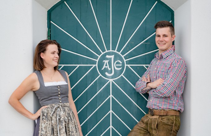 A man and a woman in traditional dress in front of a green door with a geometric pattern.