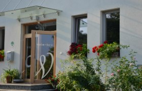 Entrance of a building with the inscription 'wein + bett', surrounded by flowers.