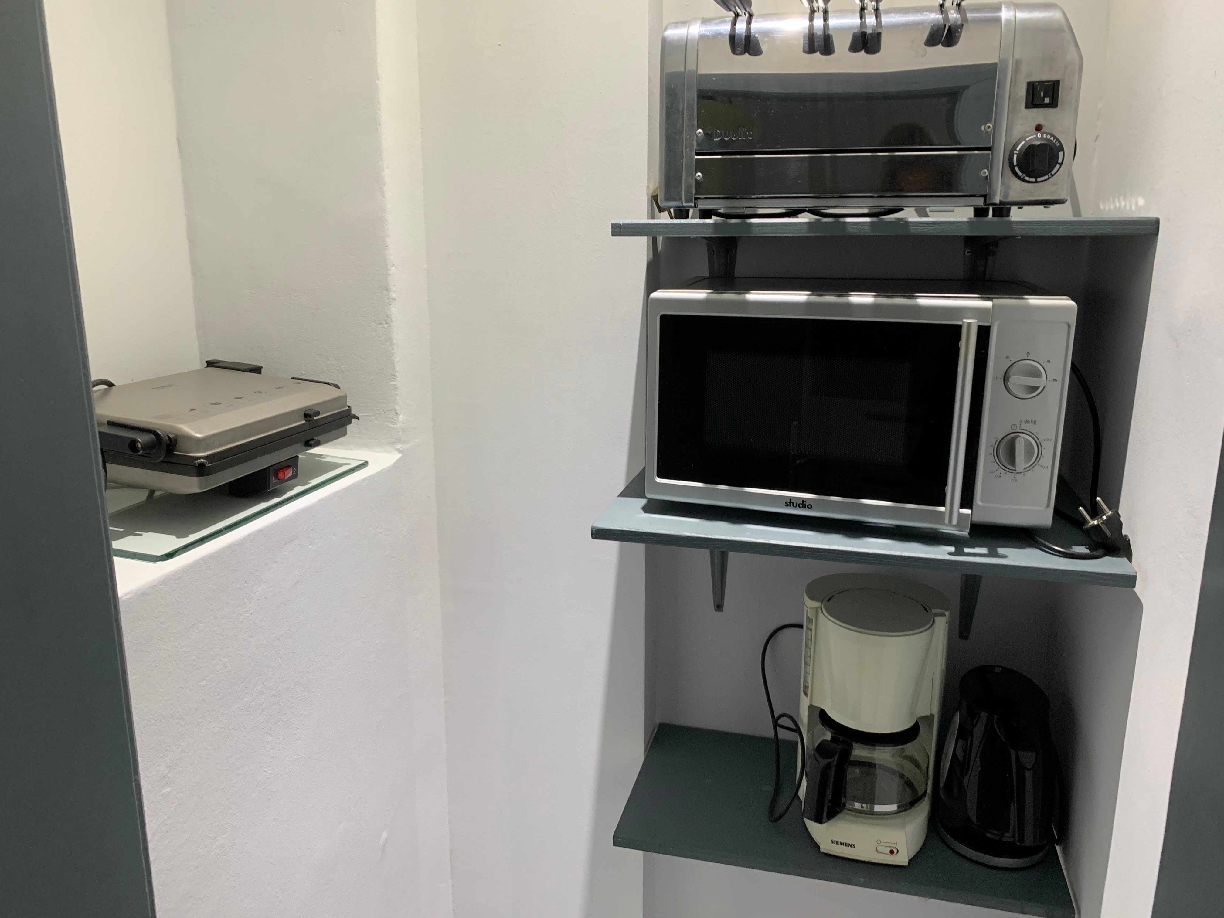 Kitchen shelf with toaster, microwave, coffee machine and kettle.