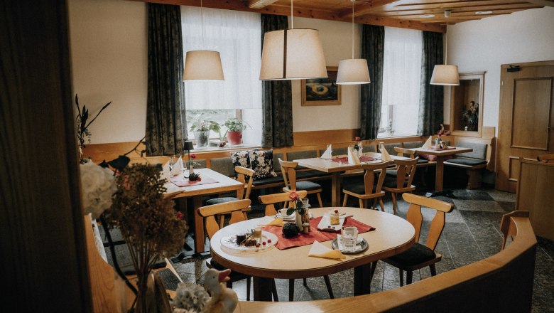 Cozy dining room with wooden furniture, set tables and hanging lamps.