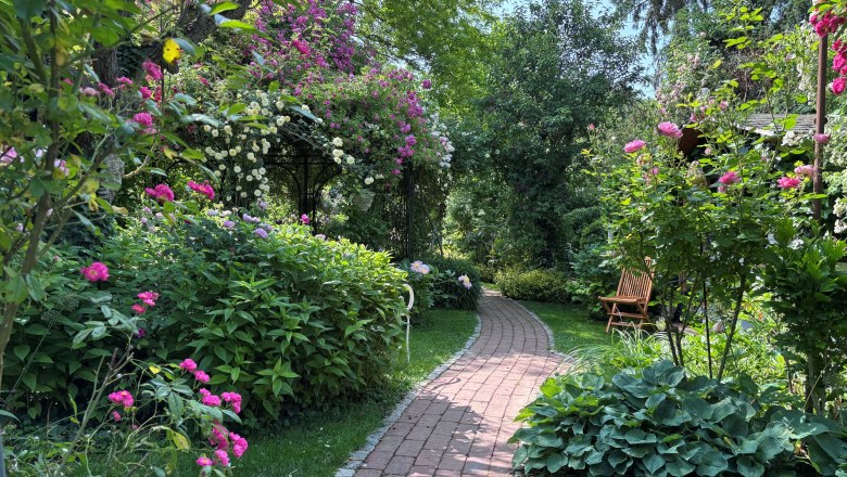 An idyllic garden with a curved brick path surrounded by lush flowers and shrubs.