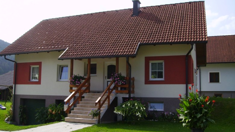 A detached house with a red roof and white and red façade, surrounded by a well-tended garden and flowers.