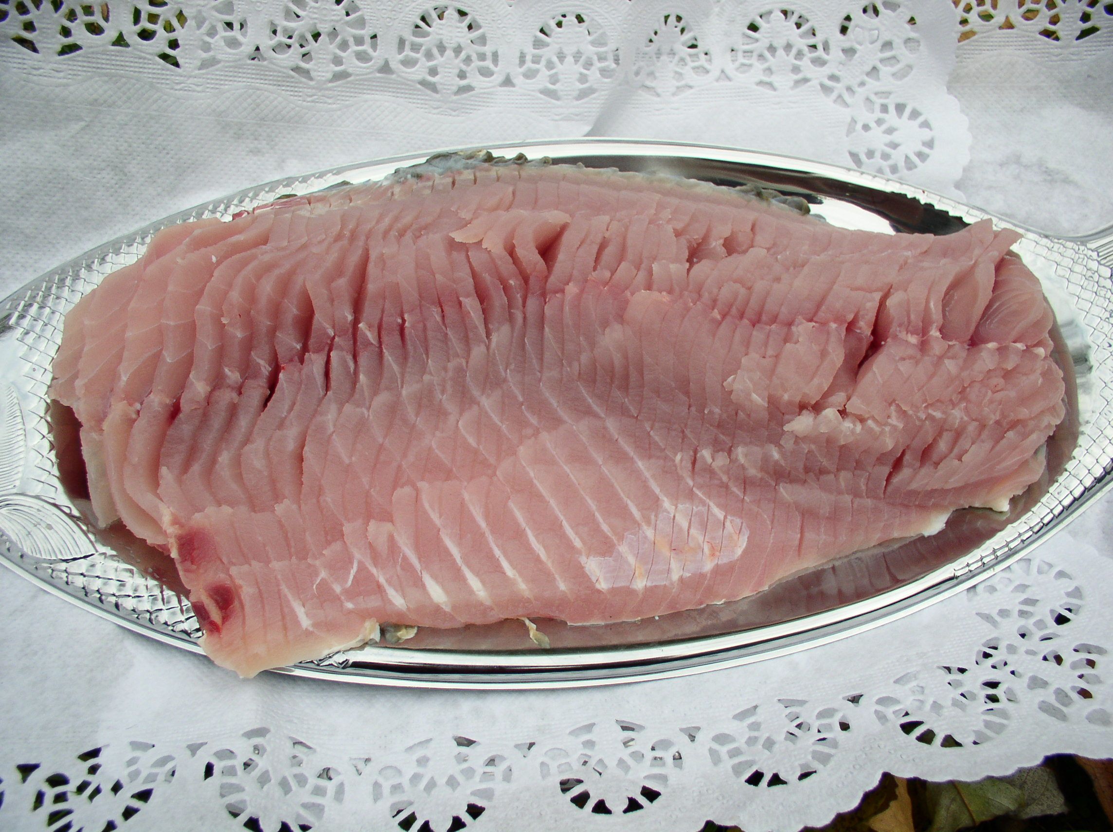 A raw carp fillet on a silver tray, surrounded by lace paper.
