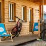 Wooden veranda with two bicycles and blue deckchairs in front of a wooden house.