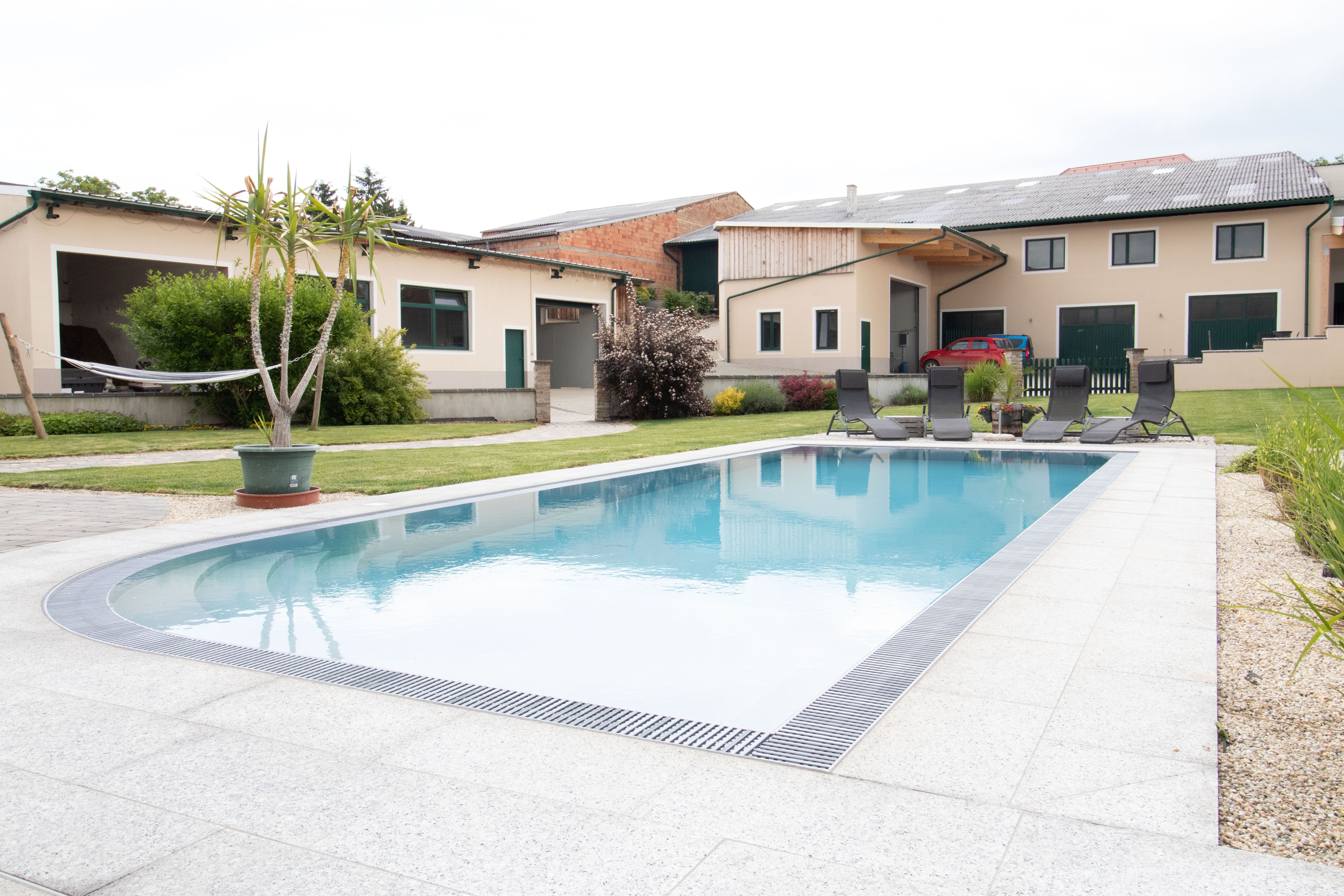 A modern courtyard with a large swimming pool and lounge chairs in the foreground.