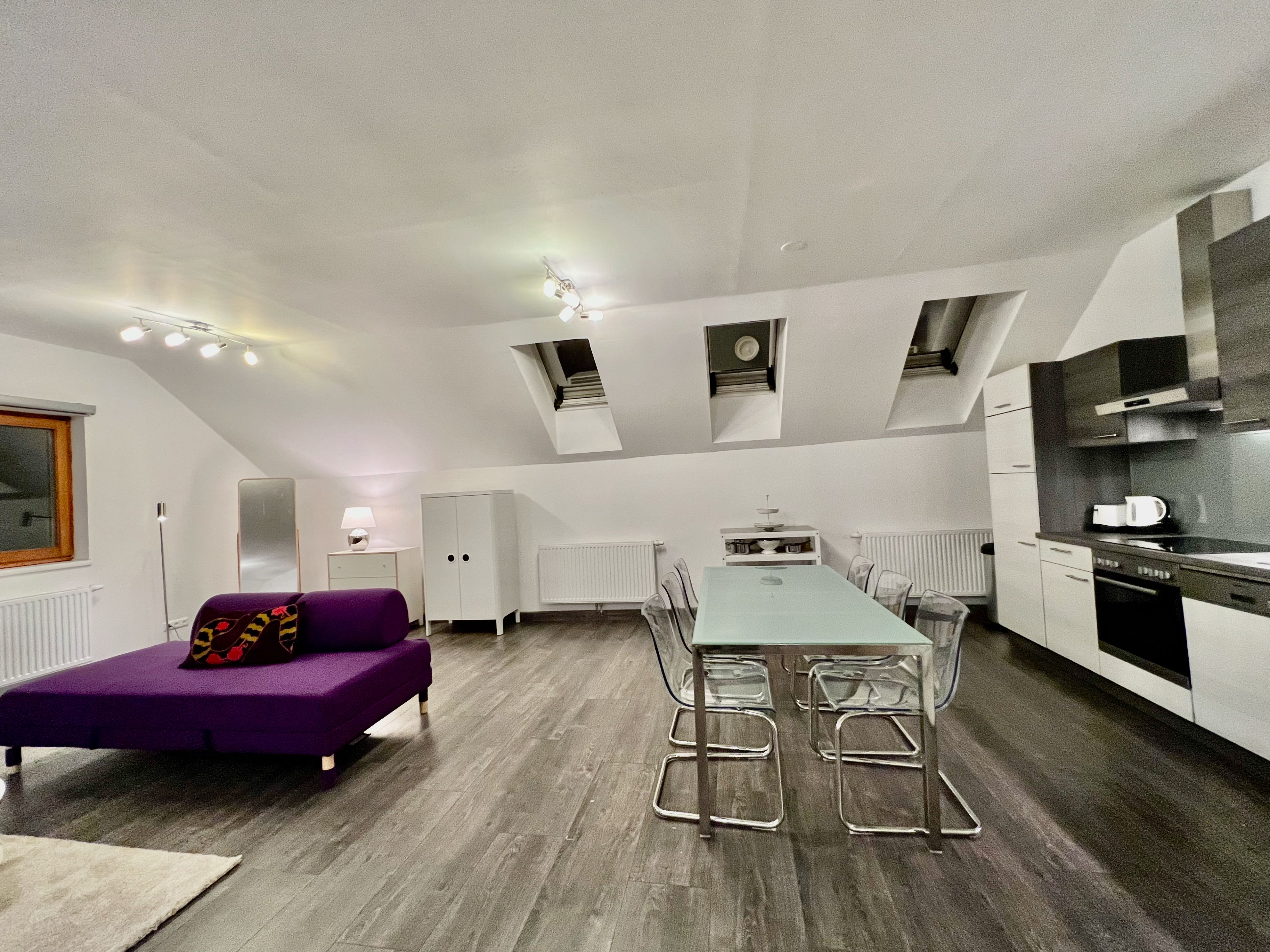 Modern loft with open kitchen, dining table and purple sofa.