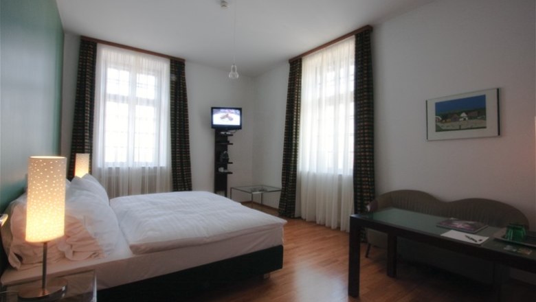 Room Grafenegg Castle, © Mörwald GmbH A hotel room with a double bed, two windows, a small TV and a table and chair.