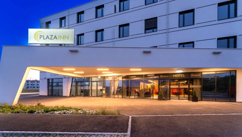 Entrance to the Plaza Inn Hotel at night with illuminated sign and modern architecture.