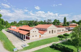 Roman town of Carnuntum with reconstructed buildings and red roofs, surrounded by green trees and lawns.