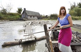 Woman on a boat in front of a ship mill on a river bank.