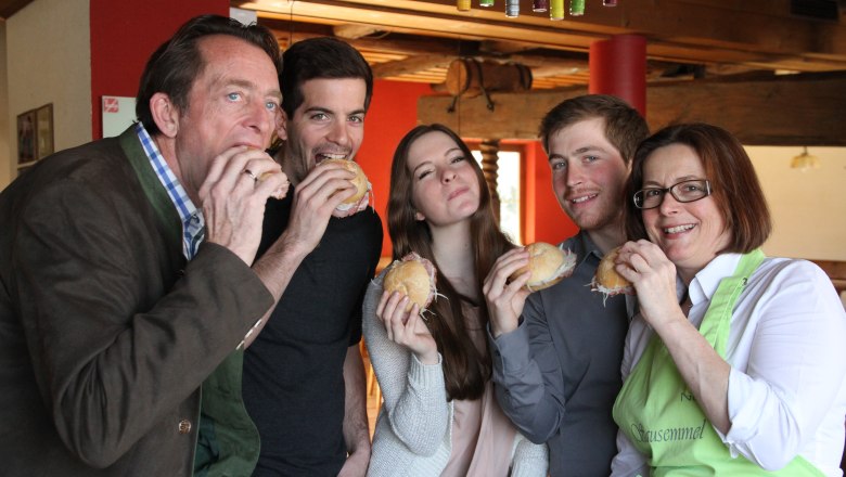 Five people eat sandwiches together in a cozy room.