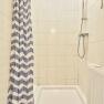 Shower with shower curtain and hand shower in a tiled bathroom.