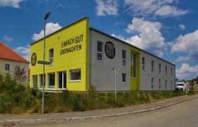 Exterior view of a modern, two-storey motel with a yellow façade and the inscription 'Einfach gut übernachten'.