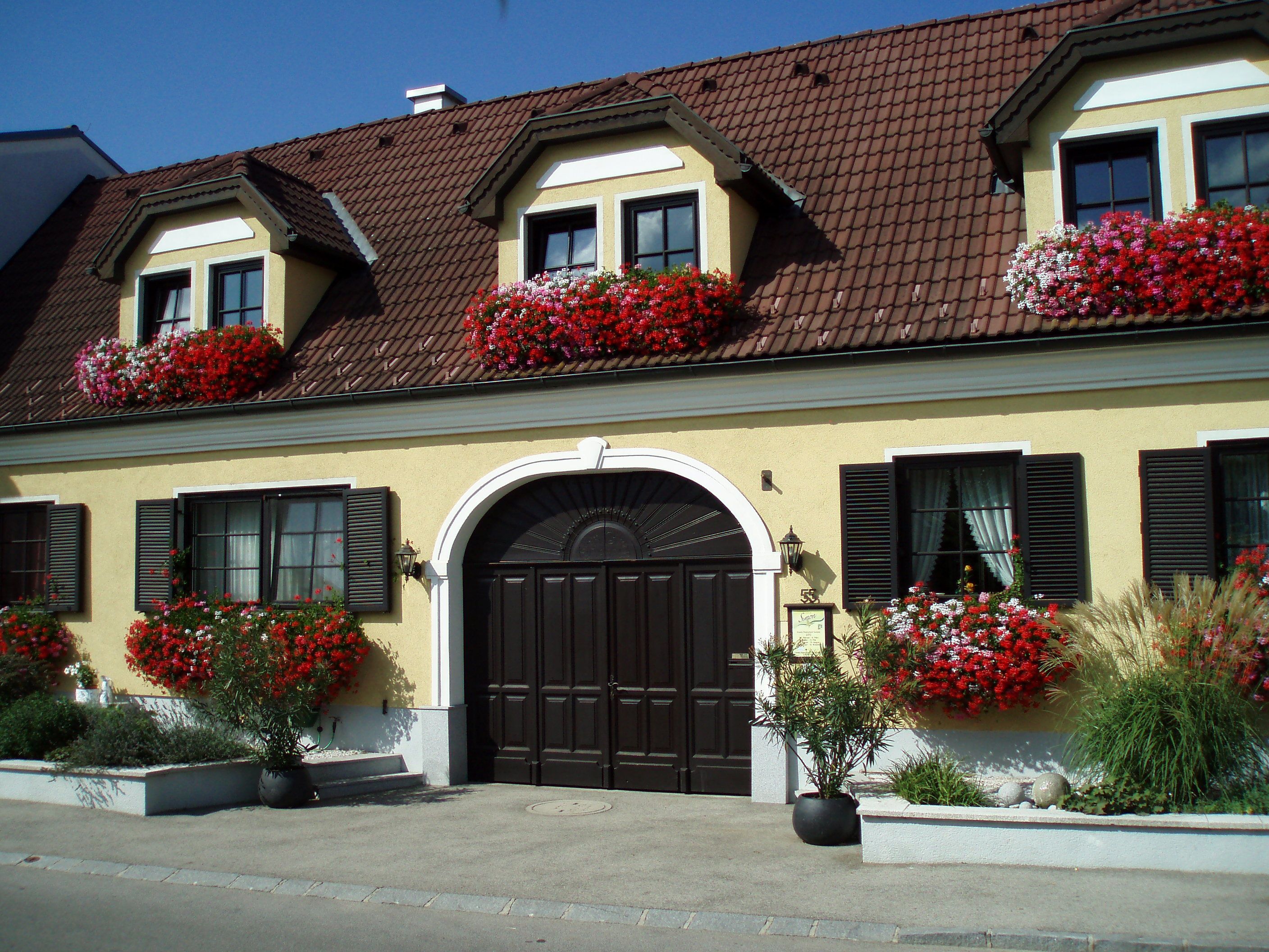 Yellow house with red flowers and brown roof.