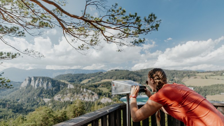 Woman looking through a viewer at a mountain landscape on the Semmering railroad hiking trail.