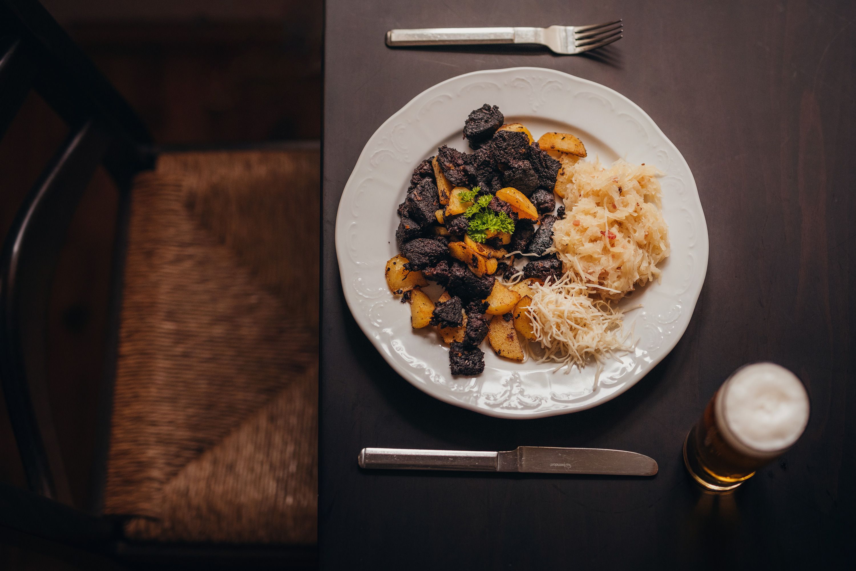 A plate with Blunzengröstl, sauerkraut and horseradish, next to a glass of beer on a dark table.