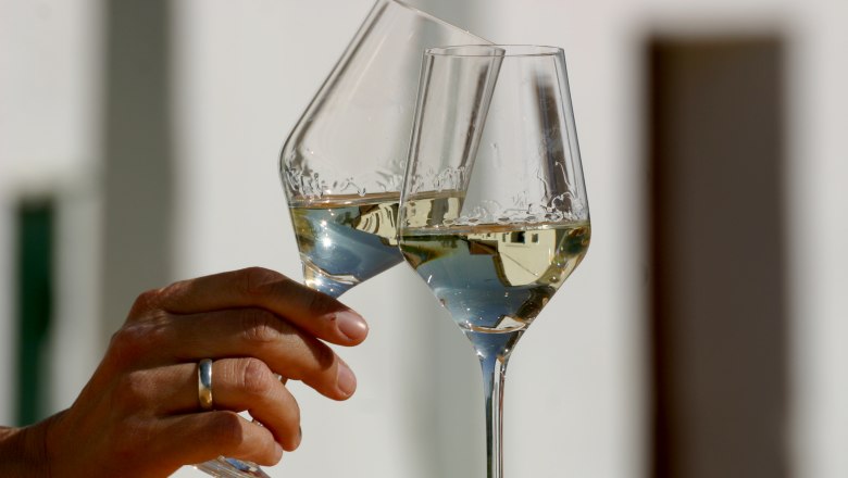 Two wine glasses toast, filled with white wine.