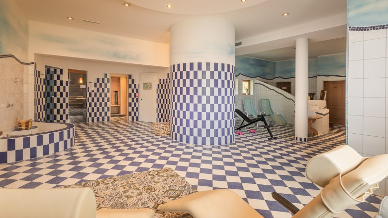 Interior view of a sauna area with blue and white checkered tiles, loungers and fitness equipment.