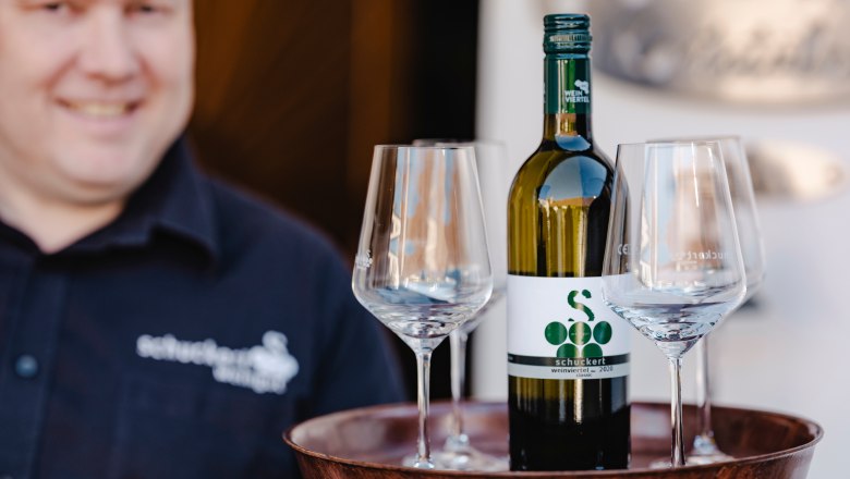 A man holds a tray with a bottle of wine and three glasses.