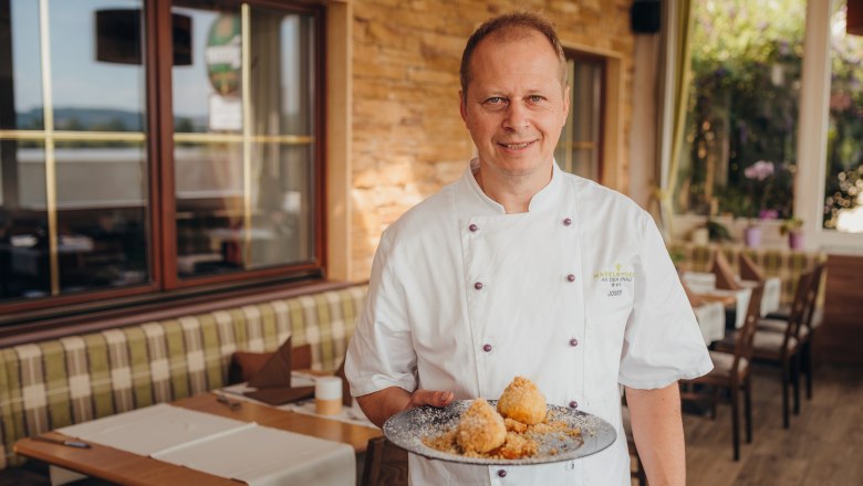 Cook in white uniform presenting plates of dumplings in a restaurant.