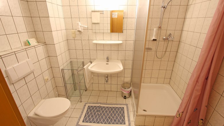 Small bathroom with shower, washbasin and toilet, tiled in white.