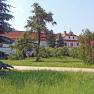 A historic building with a red roof, surrounded by trees and a green meadow.