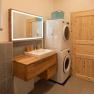 Modern bathroom with wooden washbasin, illuminated mirror, washing machine and dryer. Towels on wooden shelves.