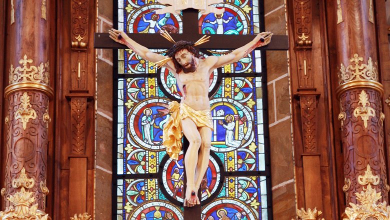 Crucifix in front of a colorful stained glass window in the collegiate church of Ardagger.