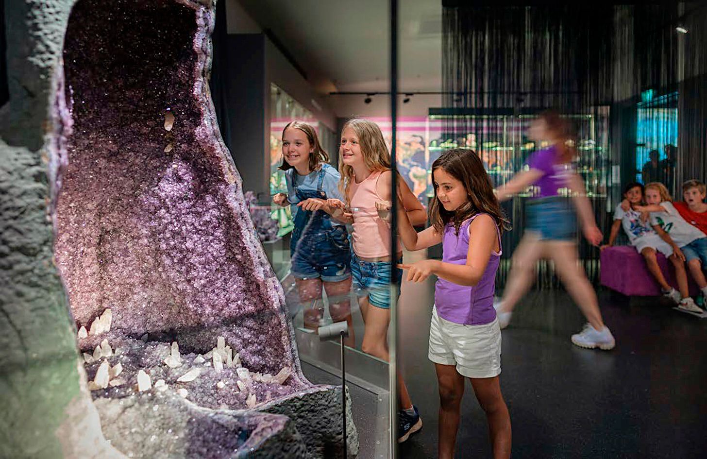 Children look at a large amethyst geode in a museum.