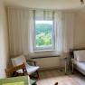 Bright bedroom with window view of green landscape, bed, chair and table.