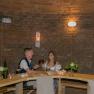 A couple sits at a wooden table in a wine cellar and toasts with red wine.