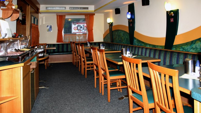 Interior view of an empty restaurant with wooden furniture and green upholstery.