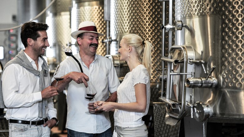 Three people at a wine tasting in a winery.