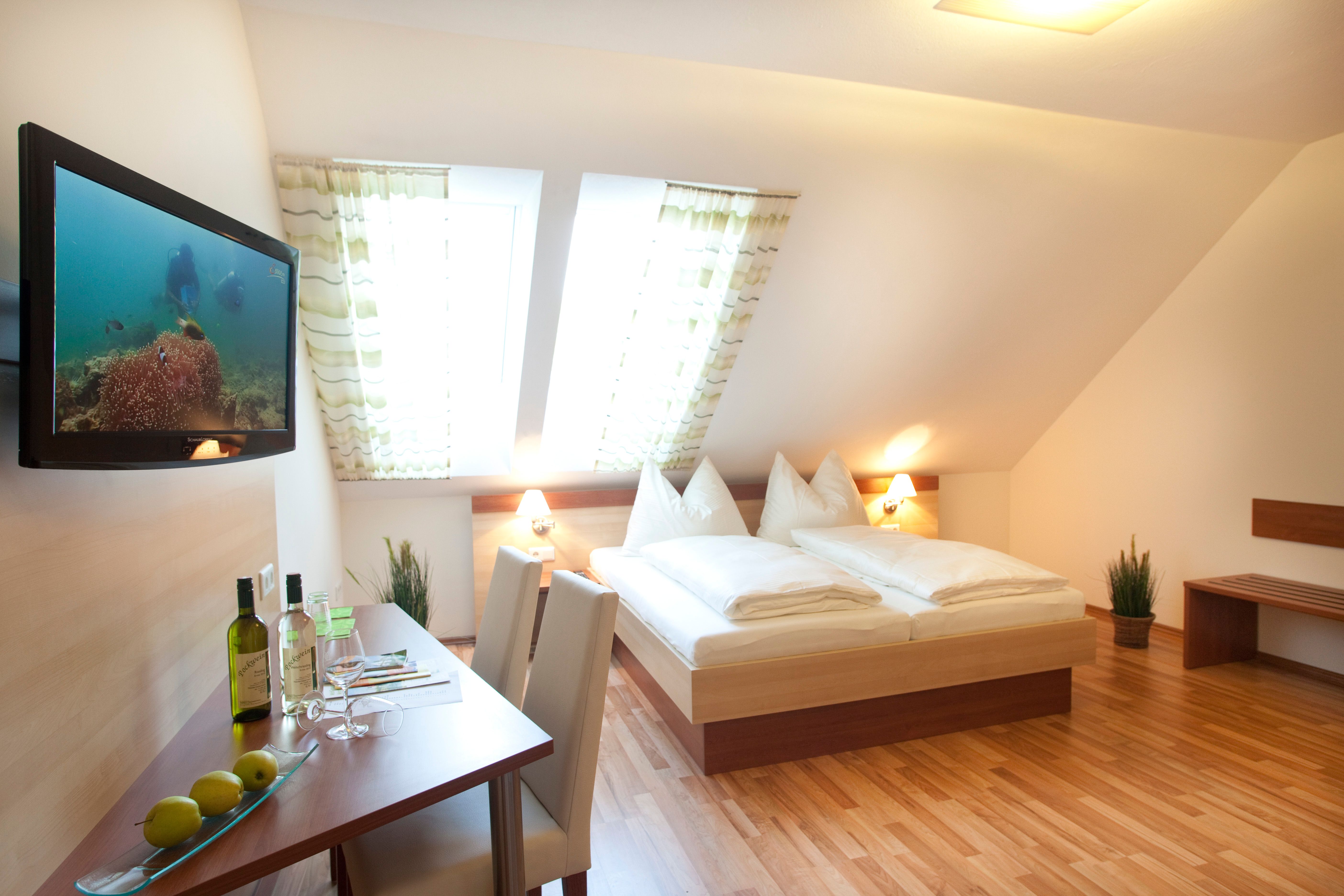 A cozy guest room with double bed, flat screen TV, table with chairs and skylights.