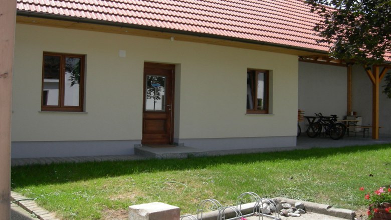 Inner courtyard, © Hörker An inner courtyard with a building with a red tiled roof, wooden door and windows. Flowers and a bicycle stand can be seen in the foreground.