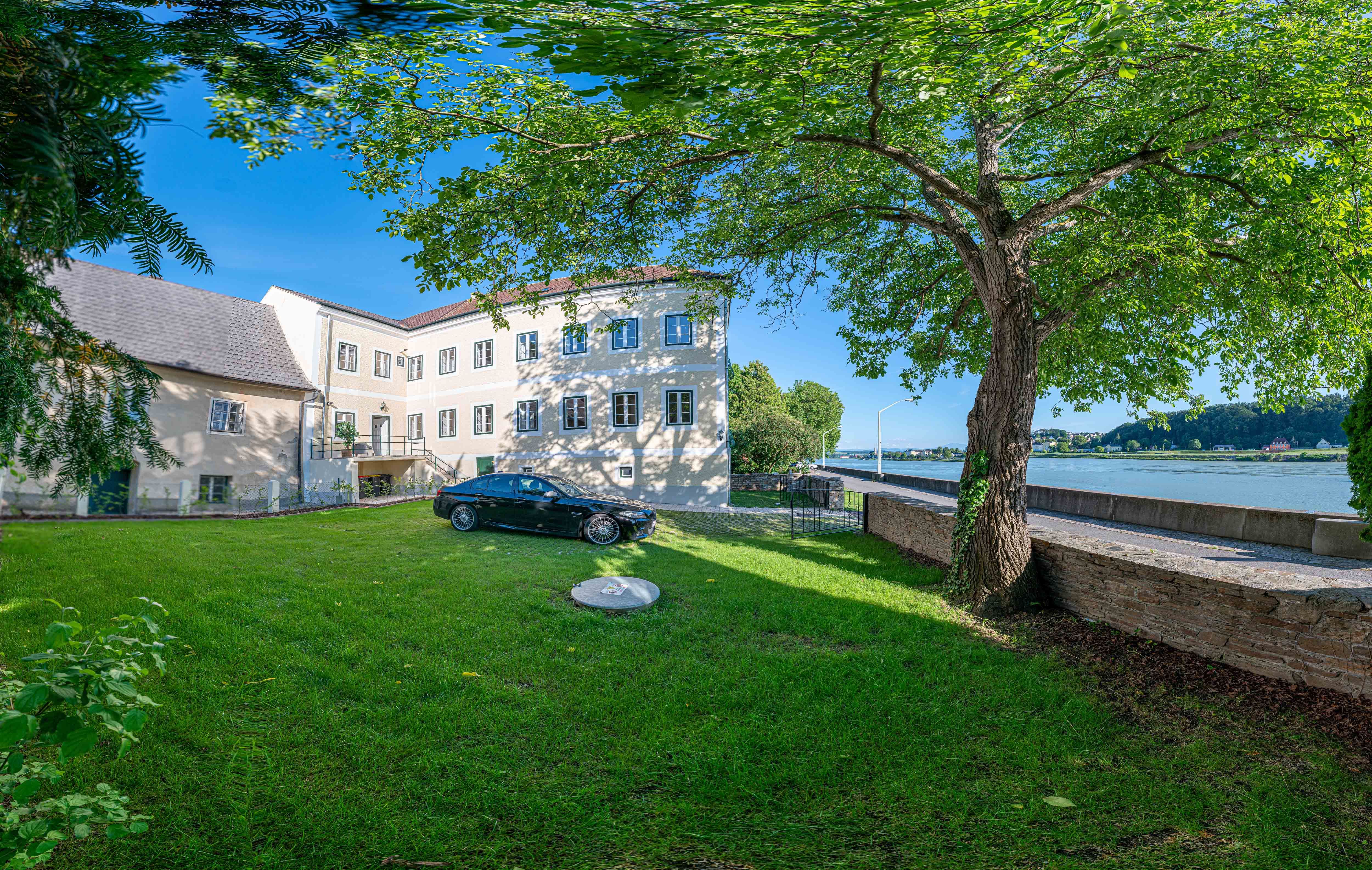 Exterior view of an old post office with tree and car in the foreground, Danube in the background.