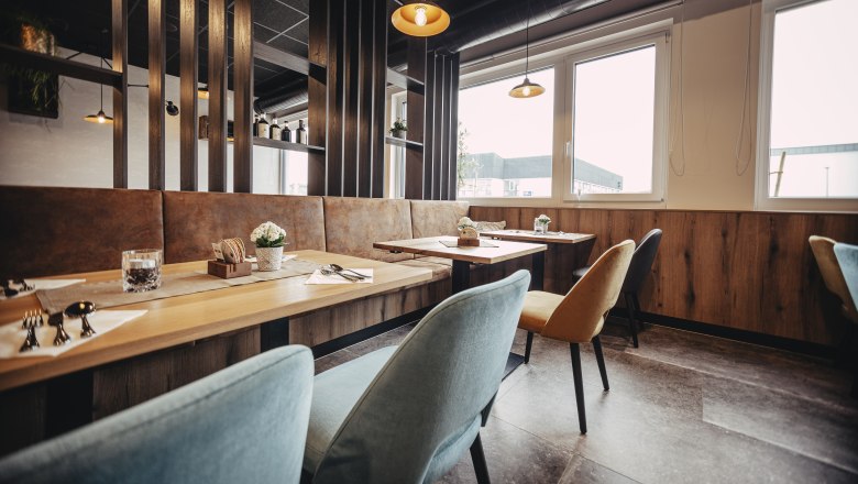 Modern restaurant with wooden tables, colorful chairs and large windows.