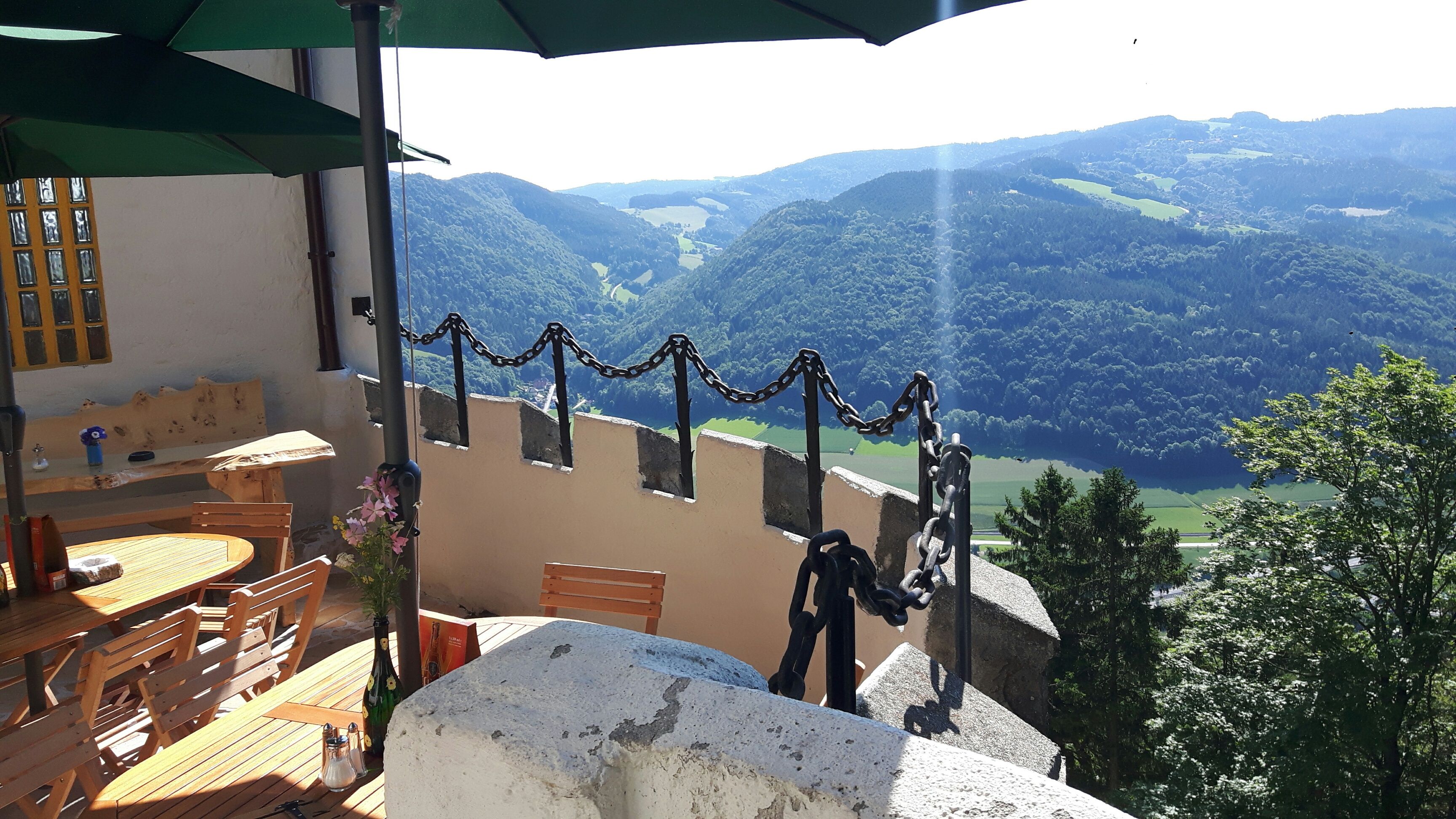 Terrace with wooden tables and chairs, view of wooded hills and valley.