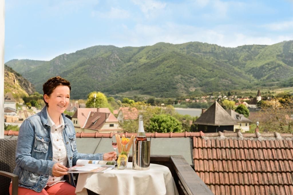 Woman on balcony with view of mountains and village.