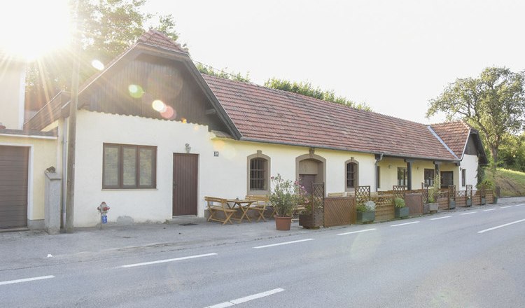 A traditional building with red tiled roofs and wooden tables in front of the door, illuminated by the sun.