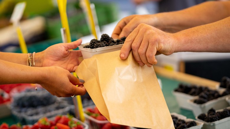 Close-up of hands handing berries into a paper bag at a market.