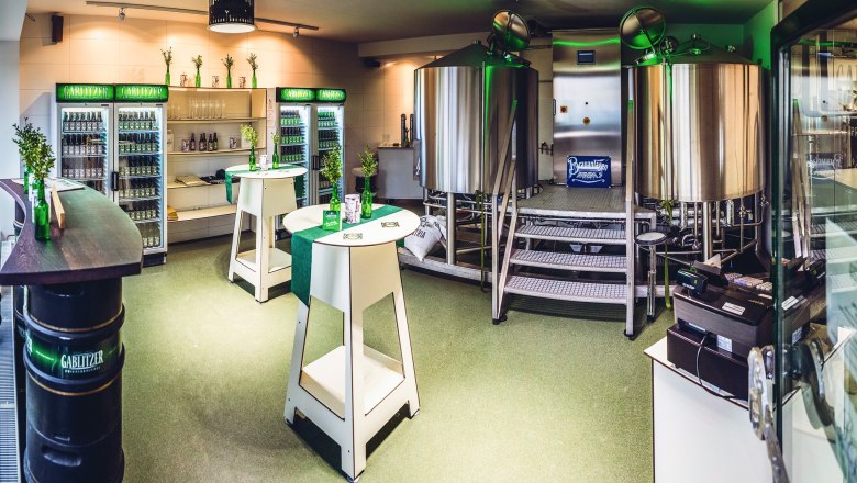 Interior view of a small brewery with stainless steel kettles and fridges full of drinks.