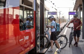 Two cyclists get on a train with their bicycles.