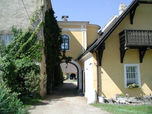 A yellow building with an archway, surrounded by ivy and a small balcony.