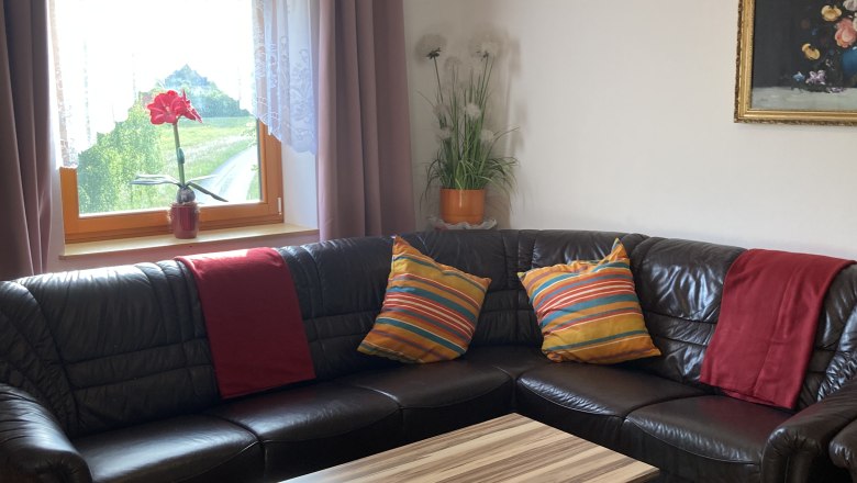 Living room with brown leather sofa, wooden table, colorful cushions and window with curtains.