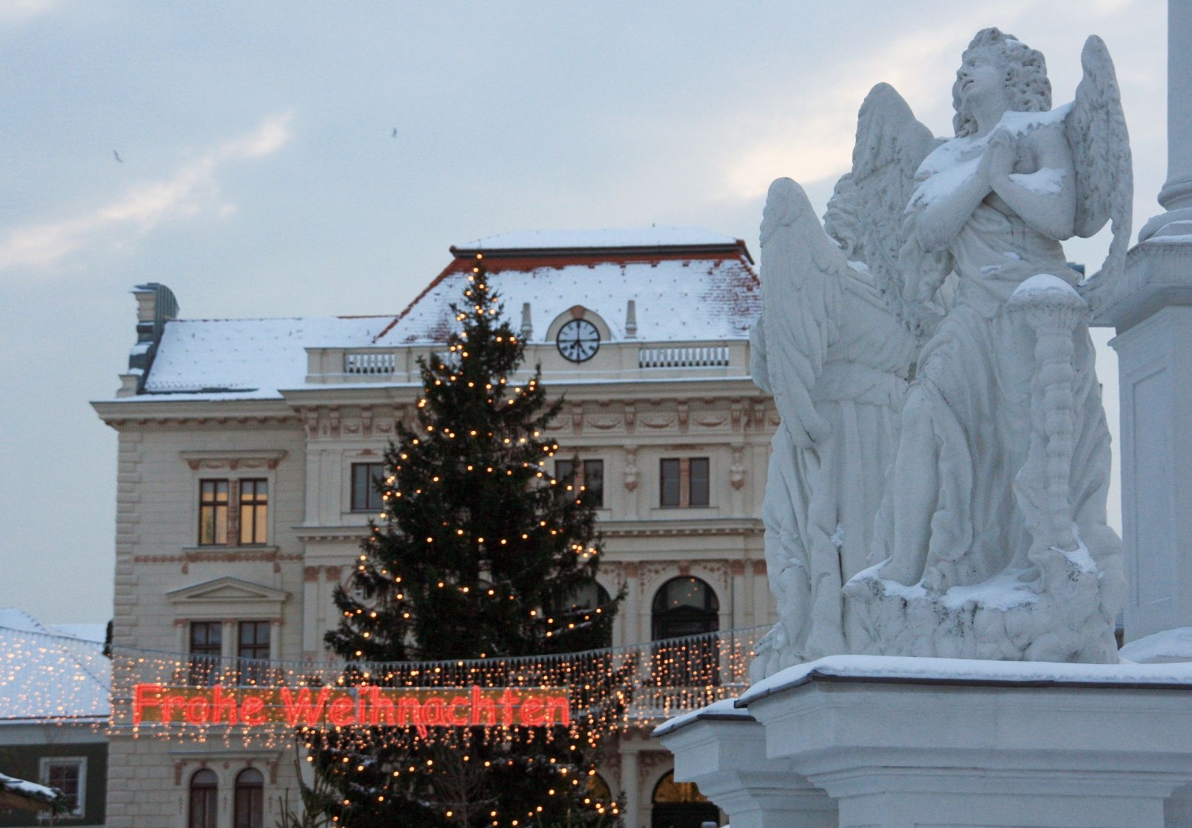 Festively decorated square with angel statue, Christmas tree and fairy lights with the inscription 'Merry Christmas'.