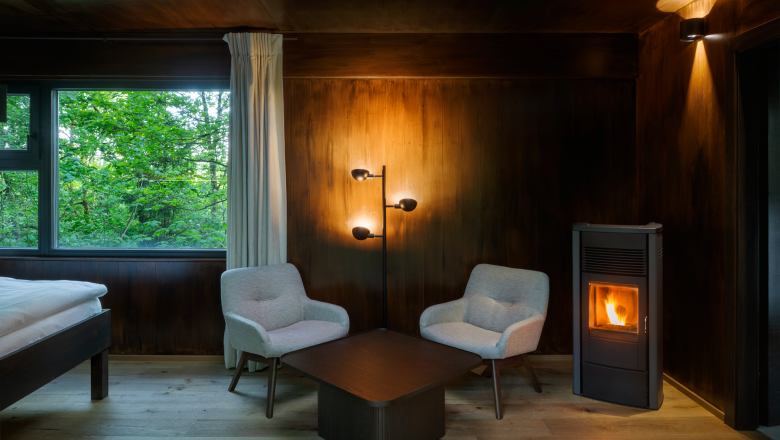 Interior view of a cozy tree house with two armchairs, a table and a wood-burning stove.