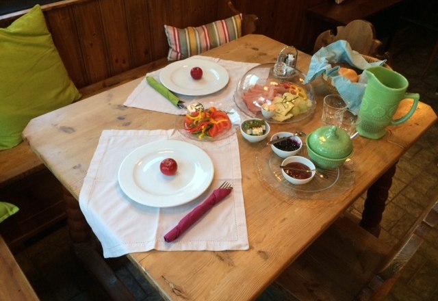 A laid breakfast table with plates, cutlery, cold cuts, vegetables and drinks.